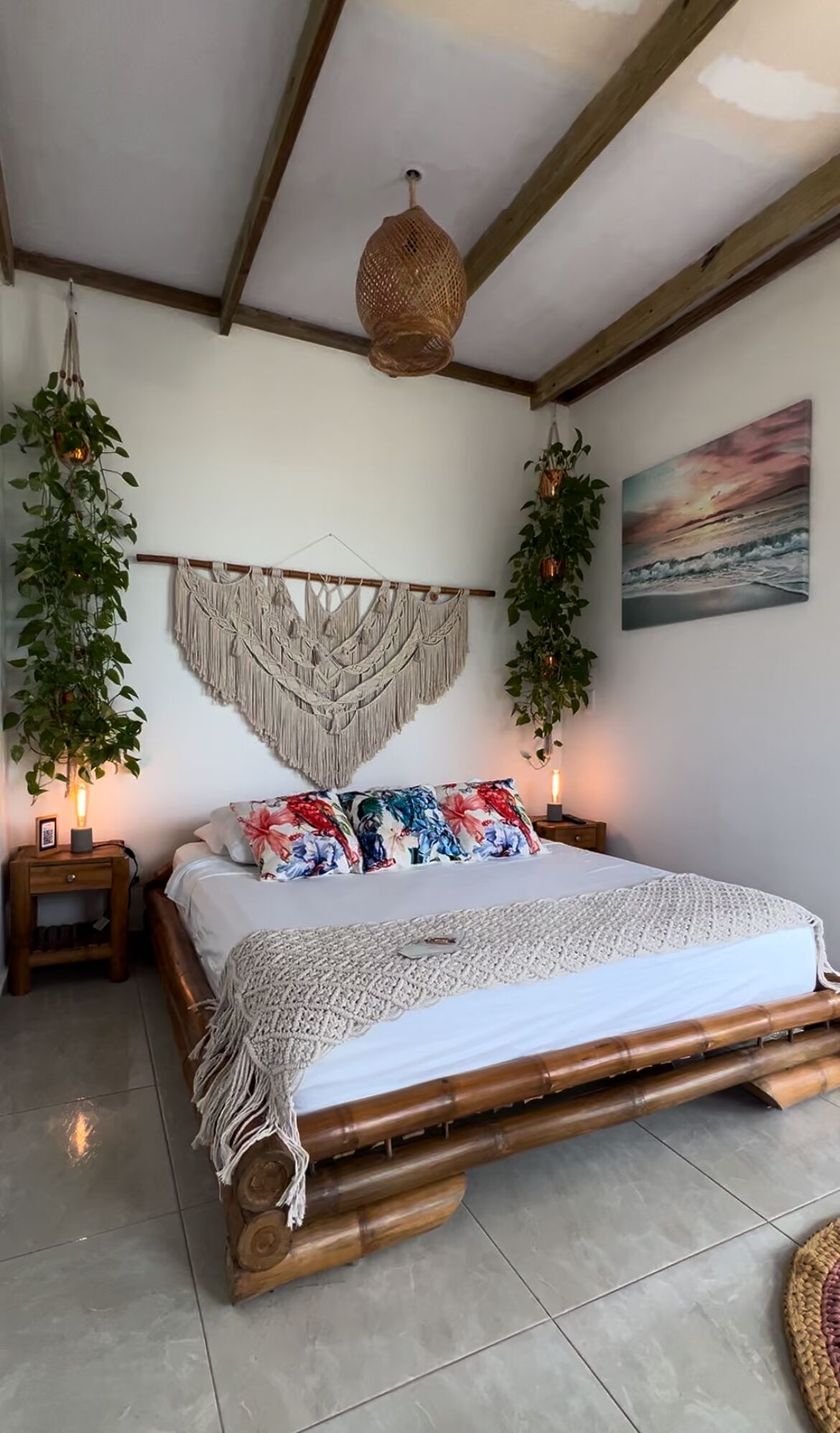 A bedroom with a bed, macramé wall hanging, hanging plants, and a painting.