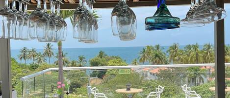 A balcony with wicker furniture, hanging wine glasses, and a view of the ocean.
