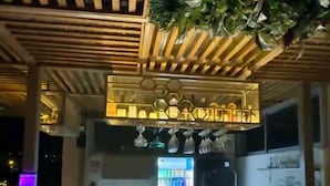 Un bar situé sur un toit, avec un panneau lumineux au néon, un plafond en bois et des plantes suspendues.