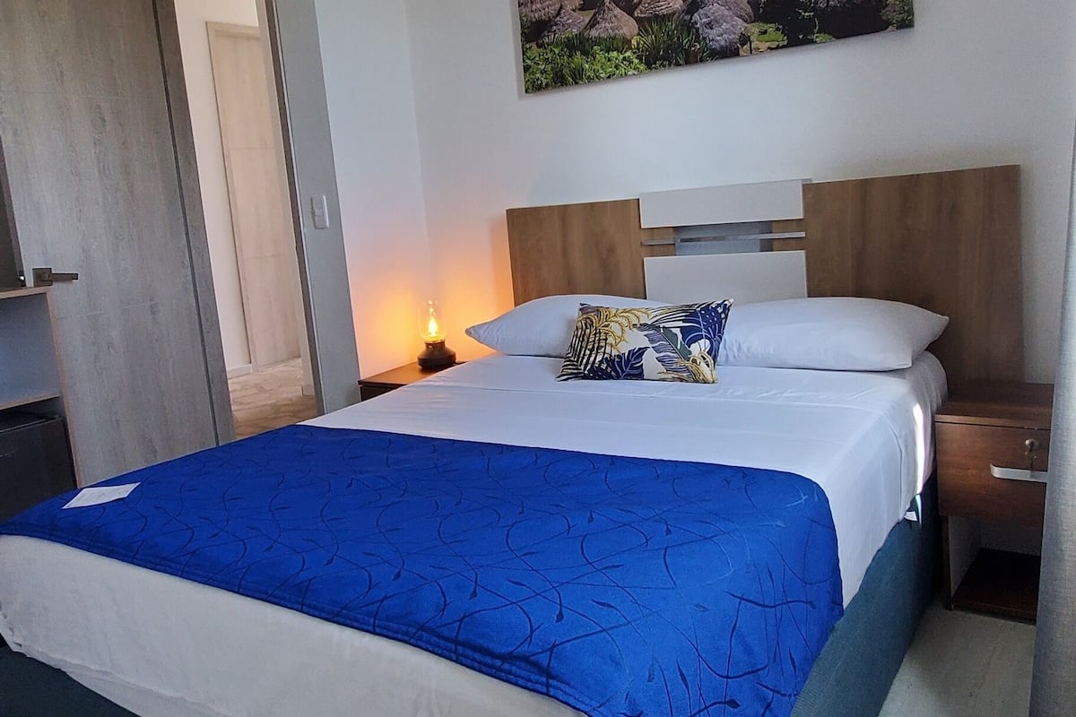 A bedroom with a bed, a nightstand, a painting, and a door.
