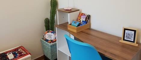A small, tidy room with a wooden desk, a blue chair, a cactus, and a framed picture on the wall.
