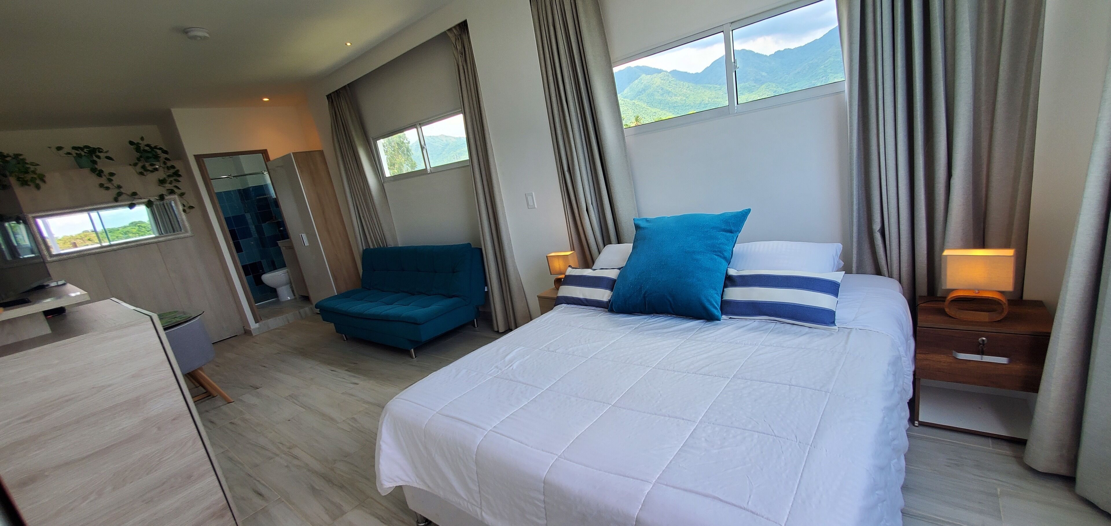 Una habitación de hotel moderna con una cama grande, un sofá, un escritorio y vistas a las montañas a través de la ventana.