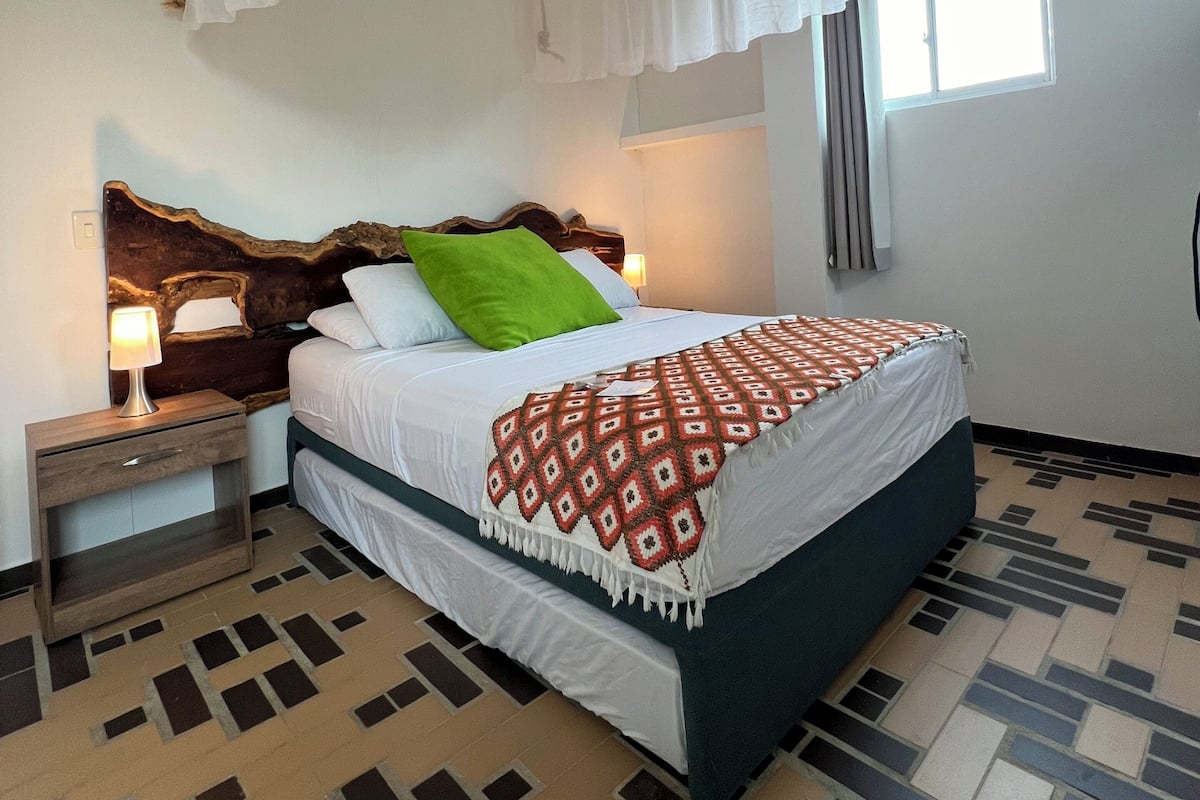 A bedroom with a bed, nightstands, a headboard, a window, and a patterned floor.