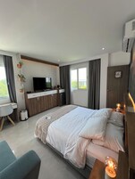 A modern hotel room with a bed, a desk, a TV, and a small kitchenette.