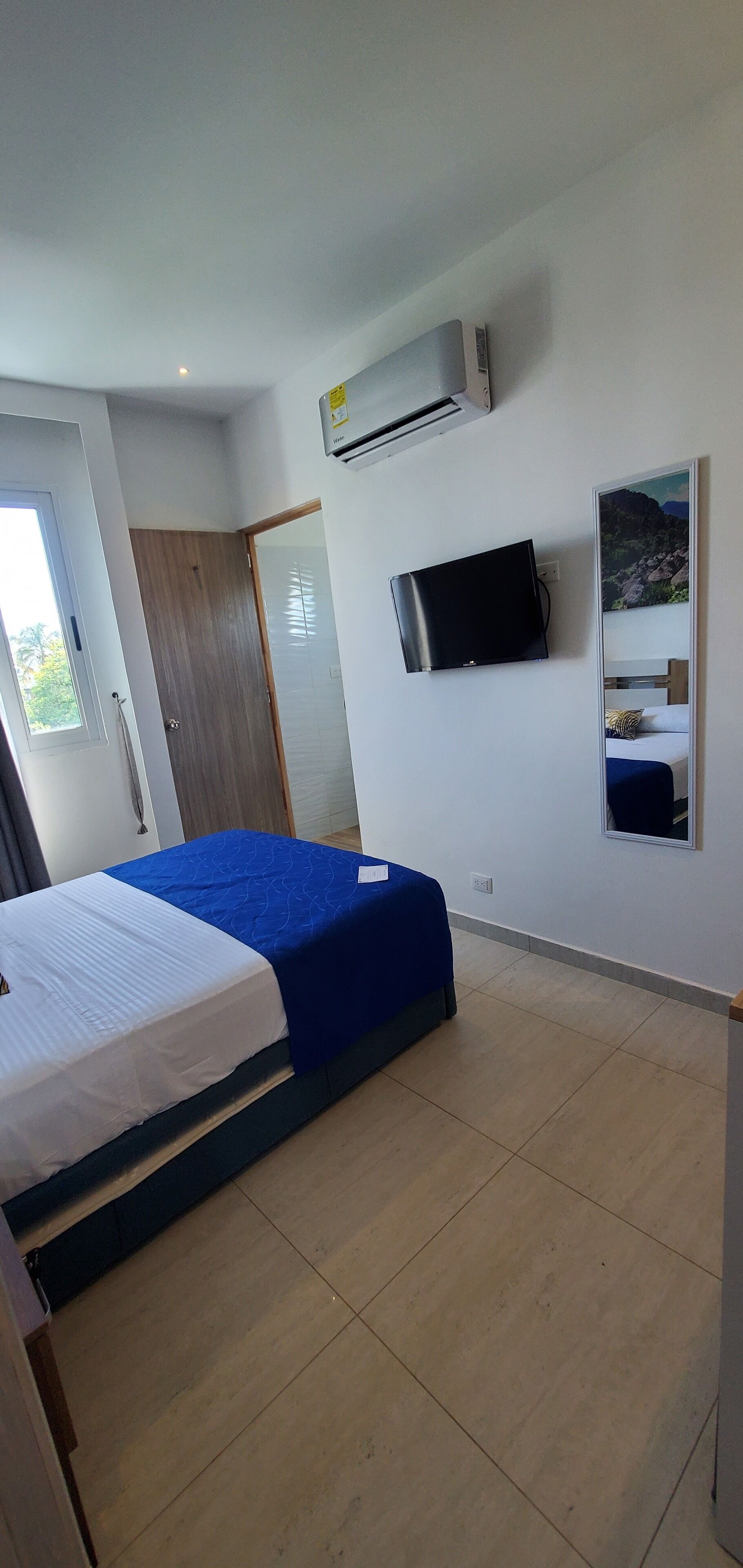 A bedroom with a bed, a TV, an air conditioner, and a door.