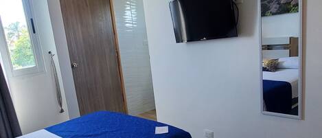 A bedroom with a bed, a TV, an air conditioner, and a door.