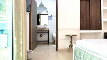 Un dormitorio con una cama grande, una mesita de noche, un espejo, un armario y un baño con lavabo e inodoro.