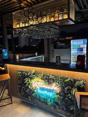 A bar area with a neon sign, a refrigerated drink dispenser, and a hexagonal light fixture above the bar. - Ritacuba House Boutique (Santa Marta)