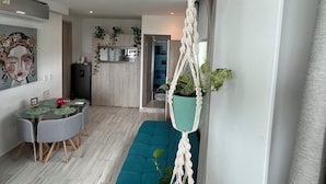 Un salon moderne avec un canapé de couleur turquoise, une table à manger avec des chaises, et une cuisine en arrière-plan.