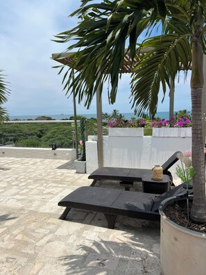 A sunlit outdoor seating area with a view of the ocean, surrounded by palm trees and potted plants. - Ritacuba House Boutique (Santa Marta)