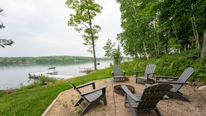 A lakeside deck with Adirondack chairs, a fire pit, and a dock extending into the water. - Lone Pine: S'mores, Sunshine, and Stanley Lake Days (Iron River)