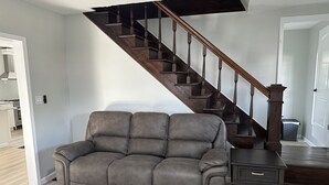 A living room with a dark brown leather sofa, a wooden staircase, and a small wooden side table.
