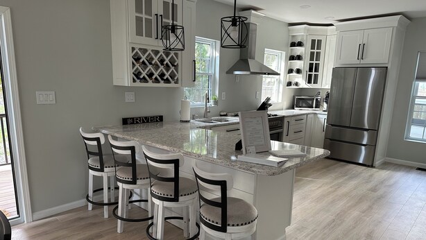 A modern kitchen with a central island, bar stools, white cabinetry, stainless steel appliances, and pendant lighting.