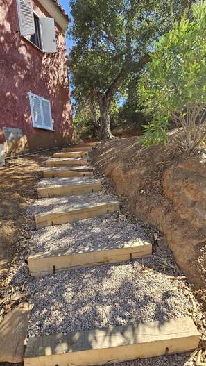 A wooden staircase with steps leading up to a building, surrounded by gravel and vegetation. - Appartement SARAH Vue mer- Clim- Wi-fi (FAVONE CONCA)
