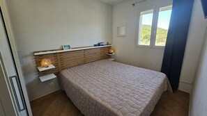A bedroom with a bed, bedside lamps, a shelf with personal items, and a window with a view. - Appartement SARAH Vue mer- Clim- Wi-fi (FAVONE CONCA)