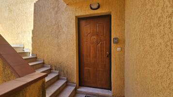 A wooden door with a circular center, a set of concrete steps leading up to it, and a wall-mounted intercom on the right.