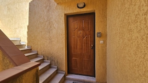 A wooden door with a circular center, a set of concrete steps leading up to it, and a wall-mounted intercom on the right. - Appartement SARAH Vue mer- Clim- Wi-fi (FAVONE CONCA)