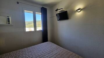 Een slaapkamer met een bed, een raam met uitzicht op heuvels en een tv aan de muur.