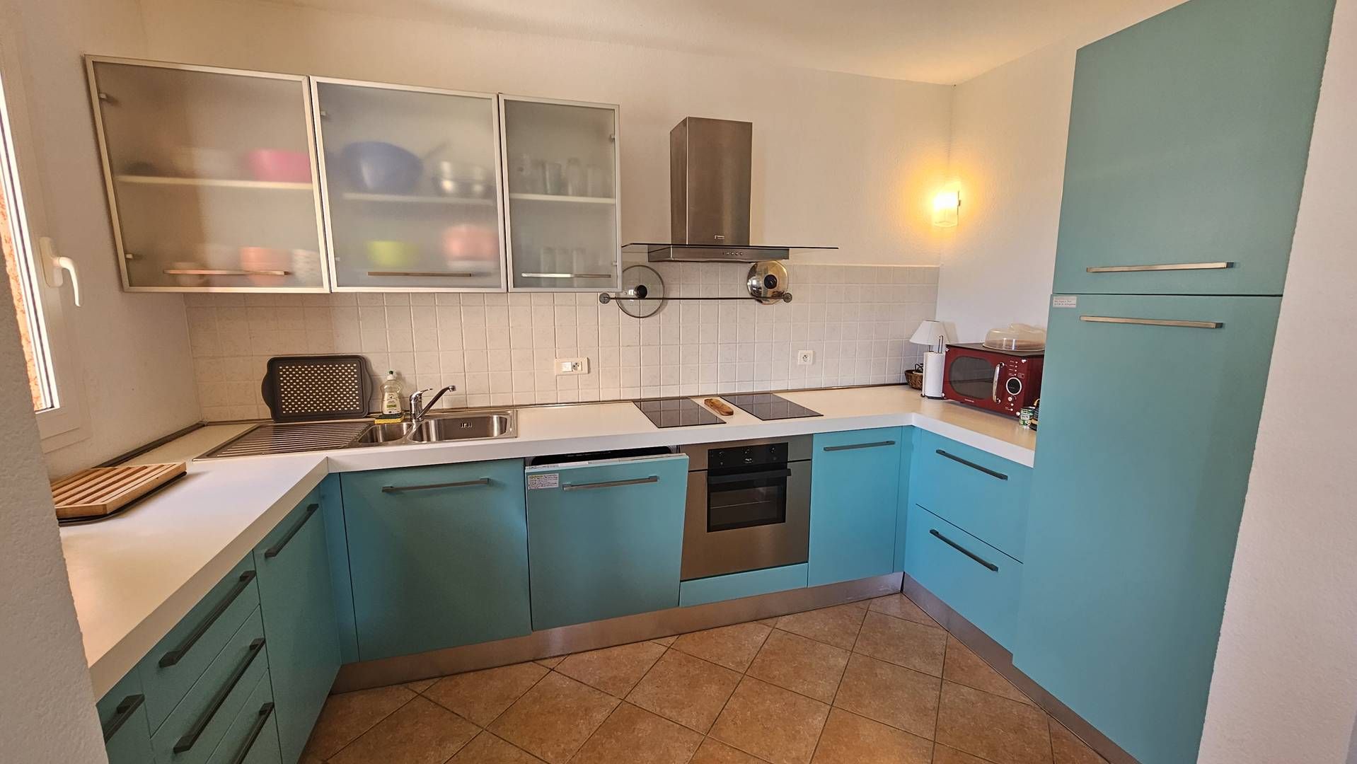 A compact kitchen with teal cabinets, a stainless steel sink, and a microwave.