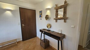 A hallway with a wooden door, a console table with decorative items, a wall-mounted mirror, and a framed picture. - Appartement SARAH Vue mer- Clim- Wi-fi (FAVONE CONCA)