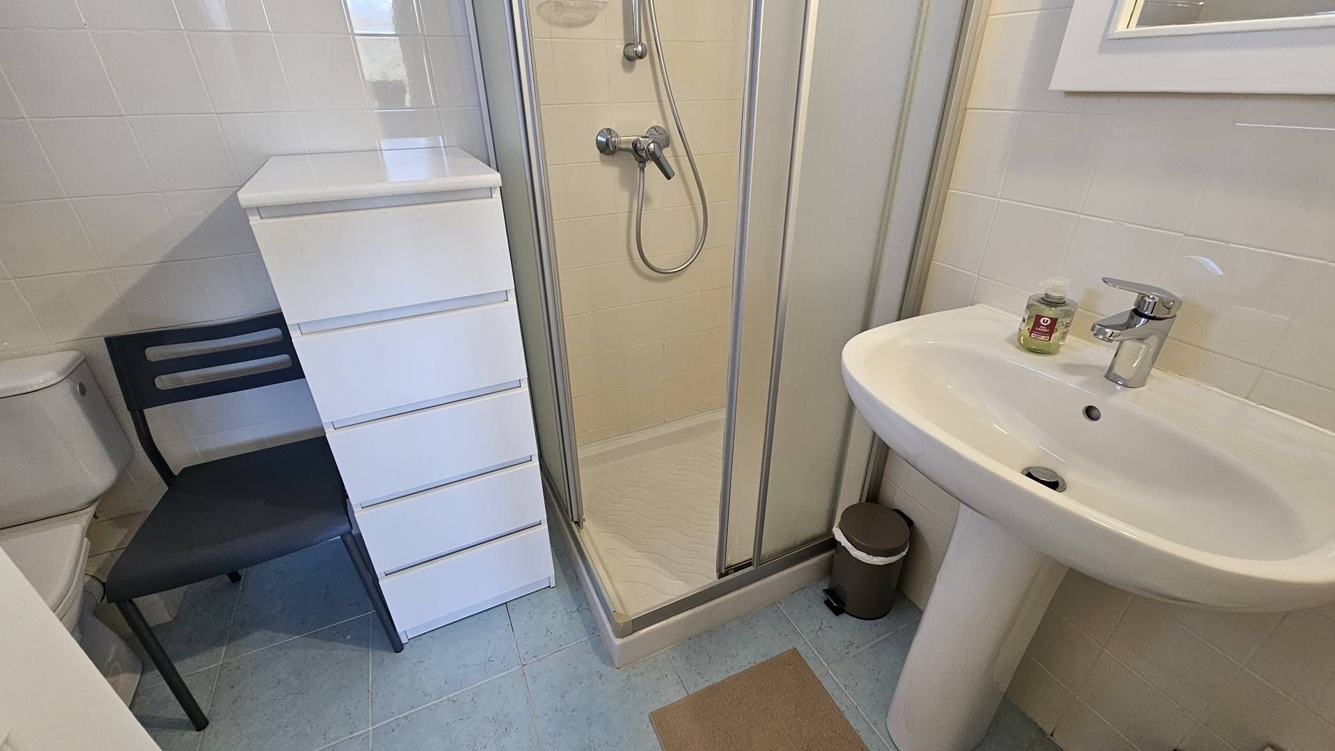 A bathroom with a shower, a sink, a toilet, and a storage unit.