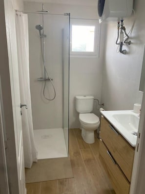 A bathroom with a glass shower enclosure, a toilet, and a sink with a mirror.