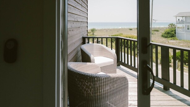 A balcony with wicker chairs, a wooden deck, and a view of the beach and ocean. - Newly remodeled condo on Wrightsville Beach steps away from the ocean!  (Wrightsville Beach)