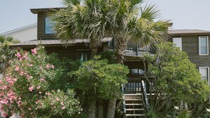 A two-story building with a balcony on the upper floor, surrounded by lush greenery and flowering plants. - Newly remodeled condo on Wrightsville Beach steps away from the ocean!  (Wrightsville Beach)