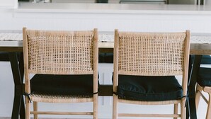 A modern kitchen with two wicker chairs, a white countertop, and a window with blinds. - Newly remodeled condo on Wrightsville Beach steps away from the ocean!  (Wrightsville Beach)
