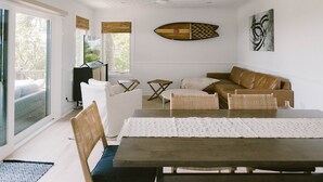 A modern living room with a dining table, wicker chairs, a brown leather sofa, and a large window with blinds. - Newly remodeled condo on Wrightsville Beach steps away from the ocean!  (Wrightsville Beach)