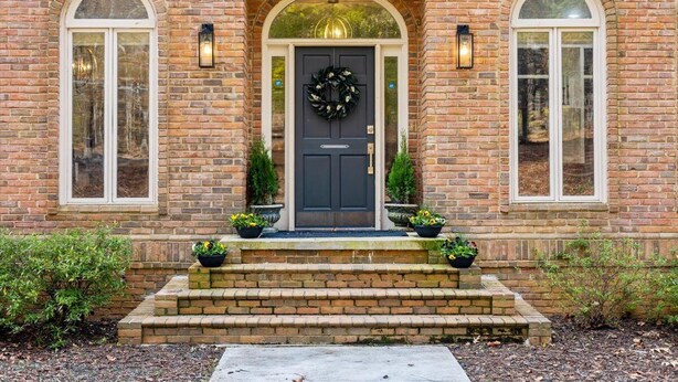A brick building with a dark front door, two arched windows, and a wreath on the door.