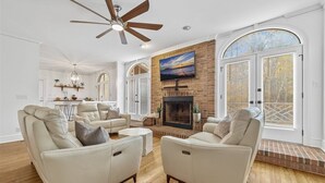 A spacious living room with a fireplace, leather sofas, and a ceiling fan.