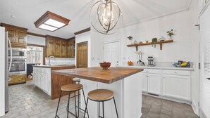 A kitchen with a central island, wooden stools, a chandelier, white cabinetry, and a window.