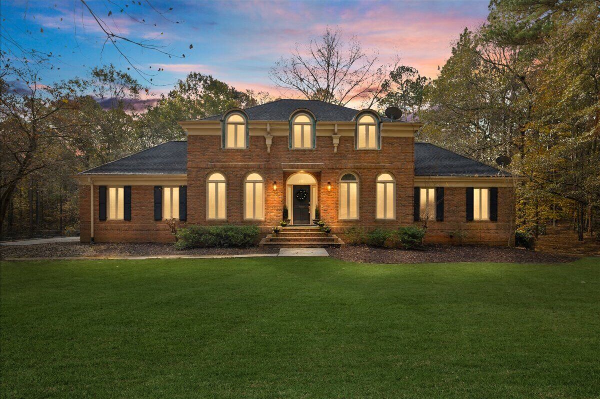 A two-story brick house with a symmetrical facade, a central entrance with steps, and a well-maintained lawn.