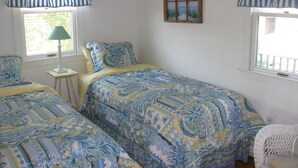 A bedroom with two beds, a window with curtains, a bedside table with a lamp, and a small painting on the wall. - Waterfront Boathouse Cottage (Falmouth)