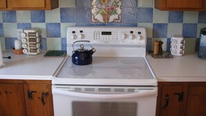 A kitchen with a white stove, wooden cabinets, and blue and green tiles. - Waterfront Boathouse Cottage (Falmouth)