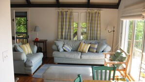 A cozy living room with a sofa, ottoman, and a wooden table with a basket. - Waterfront Boathouse Cottage (Falmouth)