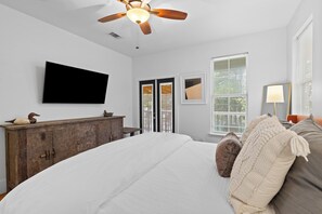 Ein Schlafzimmer mit einem großen Bett, einer Holzkommode, einem Deckenventilator, einem Flachbildfernseher und einem Fenster mit Jalousien.
