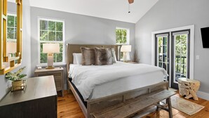 Une chambre à coucher avec un lit, des tables de chevet, un ventilateur de plafond et de grandes fenêtres.