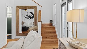 Un intérieur moderne avec un escalier, un canapé blanc, une lampe et un miroir orné d’une œuvre d’art abstraite.