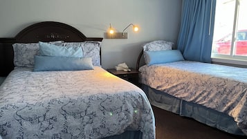 Two single beds with patterned bedding, a nightstand with a lamp, and a window with curtains.