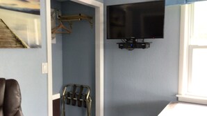 A room with a mounted television, a chair, and a coat rack. - Hitching Post Country Motel (Cornwall Bridge)