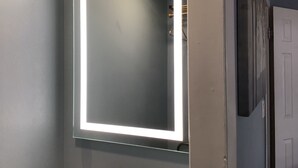 A bathroom with a large mirror, a lighted frame, and a door. - Hitching Post Country Motel (Cornwall Bridge)
