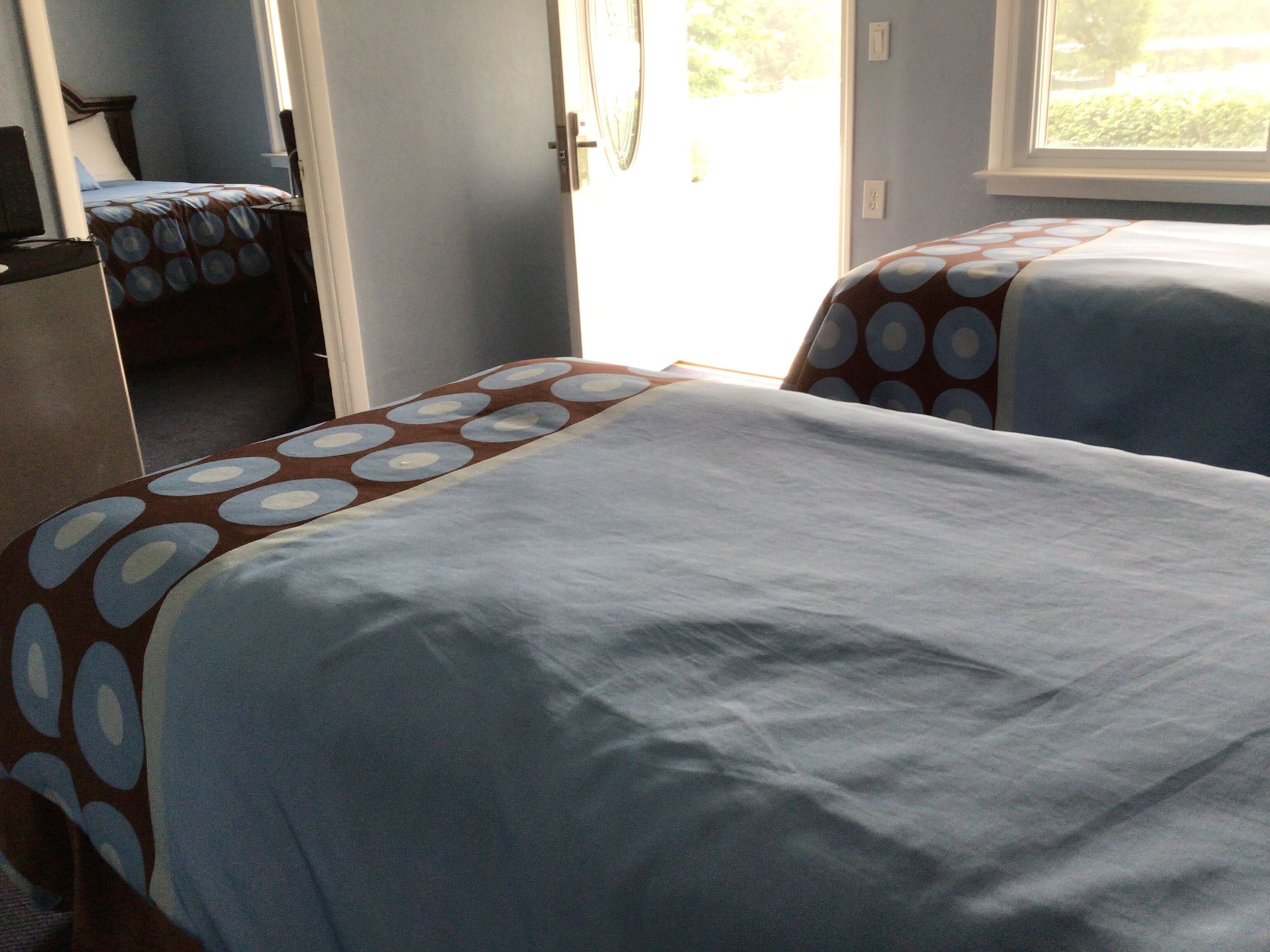 Duas camas com colchas estampadas em um quarto com janela e porta.