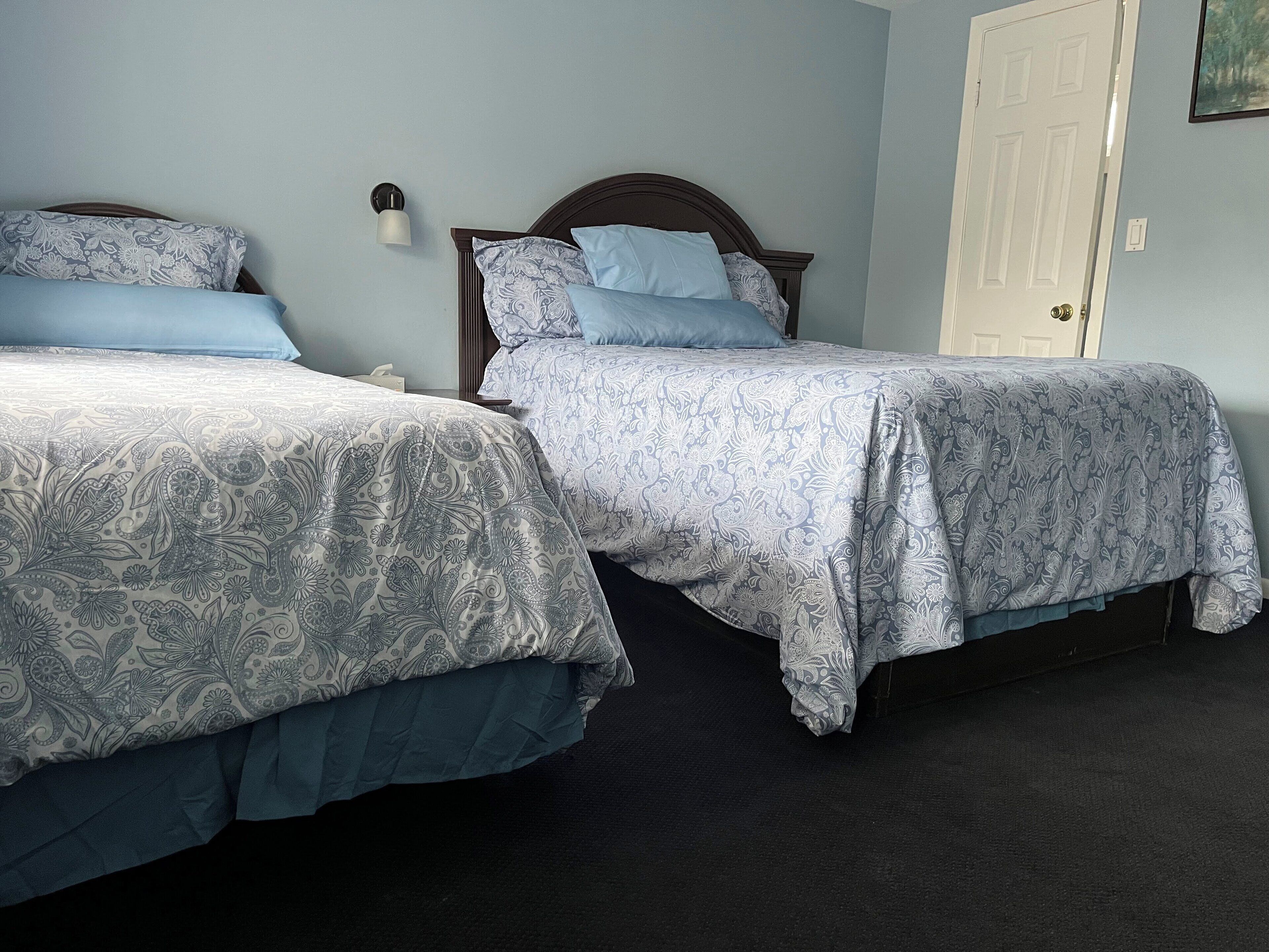 Two twin beds with matching headboards and footboards, a nightstand, a wall-mounted light, and a door.