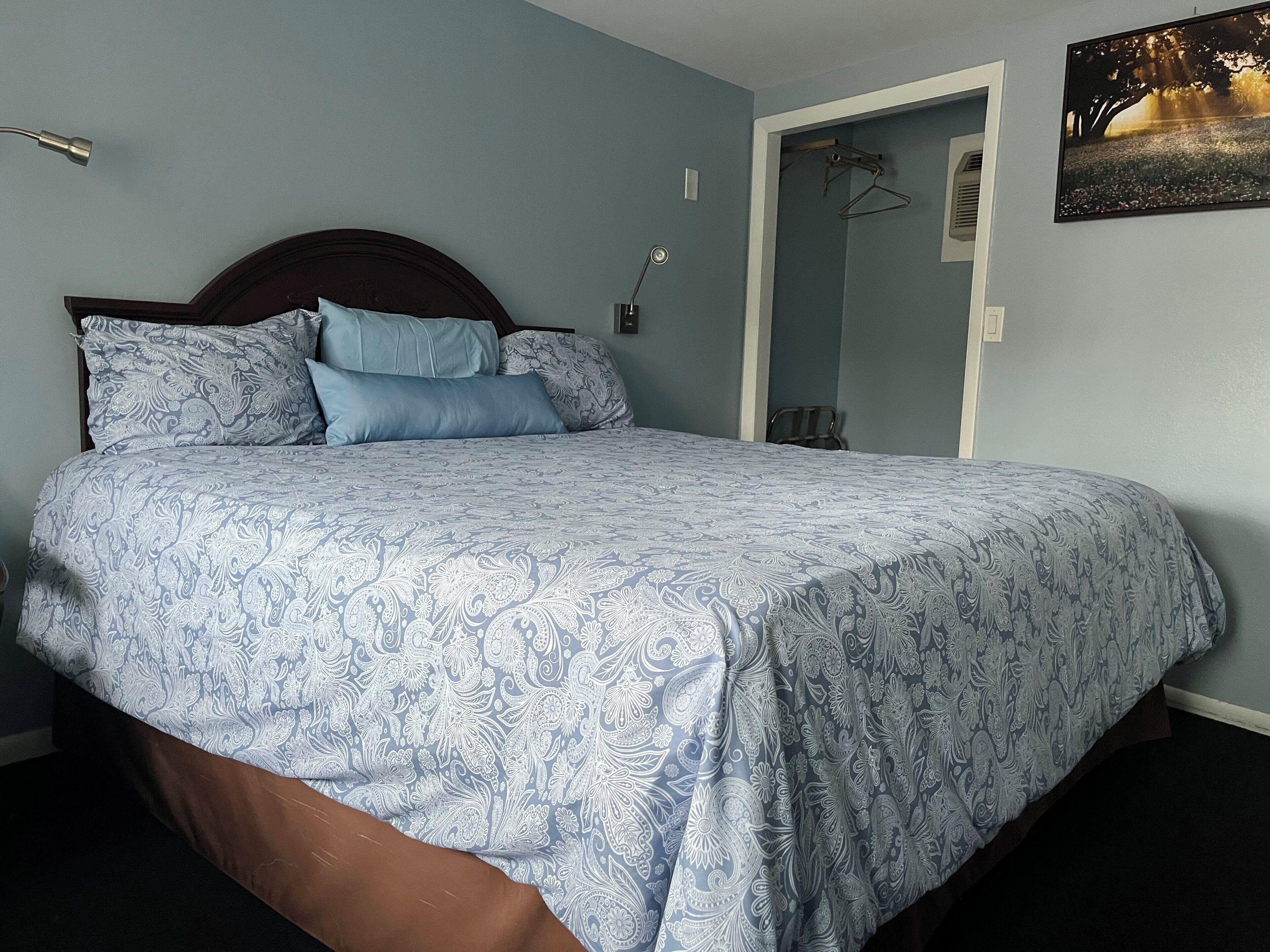 A bedroom with a bed, a nightstand, a wall-mounted lamp, and a door leading to another room.