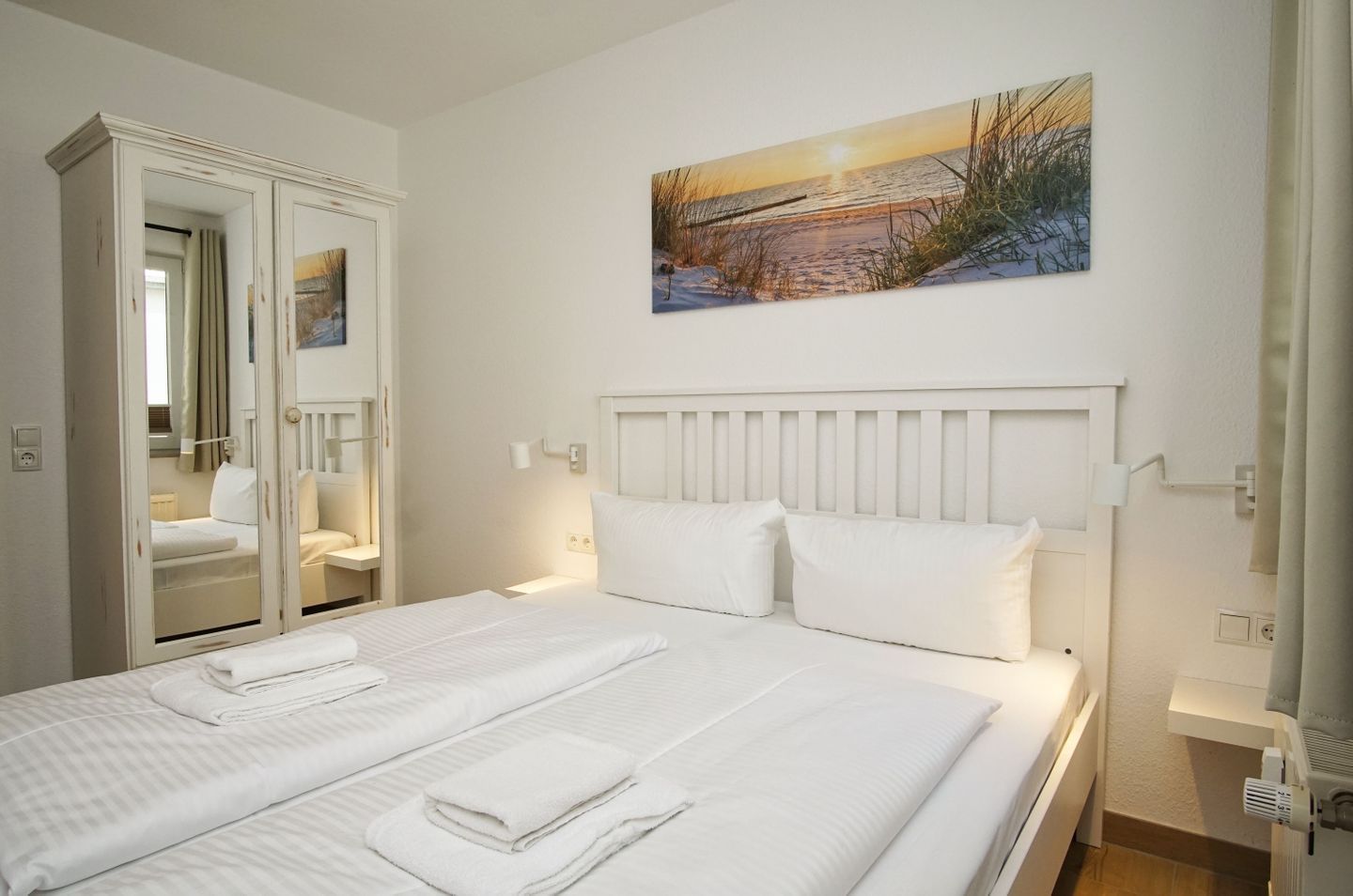 A hotel room with a bed, two bedside tables, a wardrobe, and a painting on the wall.