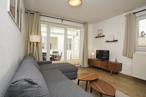 Ein modernes Wohnzimmer mit einem grauen Ecksofa, einem Holz-TV-Schrank und einem kleinen runden Tisch.