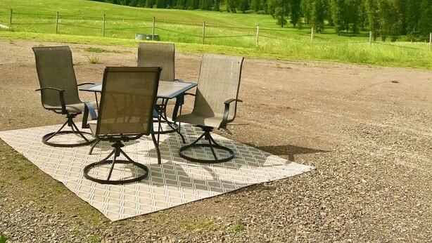 A picnic setup with four chairs and a table on a patterned mat, overlooking a grassy field and mountains under a partly cloudy sky. - The Ultimate Escape  (Heron)