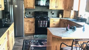 A kitchen with wooden cabinets, a stainless steel refrigerator, a microwave, a stove, and a sink. - The Ultimate Escape  (Heron)
